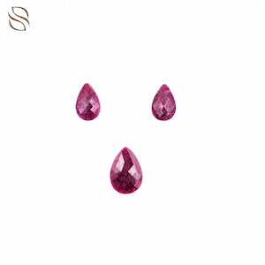 May include: Three loose, pear-shaped gemstones with a deep magenta-red hue and a faceted surface. The stones are arranged in a triangular formation, with two smaller stones positioned above one slightly larger, central teardrop-shaped gemstone.