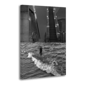 May include: Black and white photograph of a person standing on a concrete structure in the middle of a body of water. The background features an escalator and architectural elements. The image has a surreal, dreamlike quality.