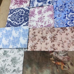 May include: Selection of fabric swatches showcasing floral and toile patterns in blue, pink, and brown hues. The fabrics display intricate designs, such as roses and classical scenes, ideal for home decor or craft projects.