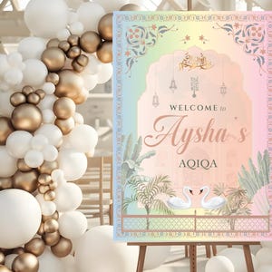 Könnte beinhalten: Ein Schild mit einem pastellfarbenen Regenbogenbogen-Design mit der Aufschrift "Welcome to Aysha's AQIQA". Das Schild zeigt Illustrationen von Schwänen und Pflanzen. Es wird auf einer Staffelei mit einem Ballonbogen im Hintergrund präsentiert.