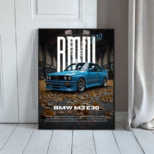 May include: A framed poster featuring a blue BMW M3 E30 car. The car is parked on a surface covered in autumn leaves. The poster has the text "BMW M3 E30" in white at the bottom and "M3 E30" at the top.