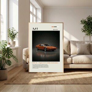 May include: Framed poster featuring an orange BMW M1 sports car. The poster has a cream-colored background with the text "M1" and "BMW" at the top. Below the car is the text "BMW M1 - Engineered to Define Performance".