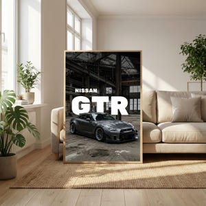 May include: Framed print featuring a gray Nissan GTR sports car. The car is parked in an industrial setting, with the word "GTR" in large white letters. The text "NISSAN" is above the car's name. The print is in a wooden frame.