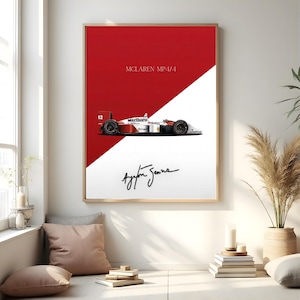 May include: A framed print featuring a McLaren MP4/4 race car design. The artwork has a red and white color scheme, with the car's side profile displayed. The print includes the text "McLAREN MP4/4" and the signature of Ayrton Senna.