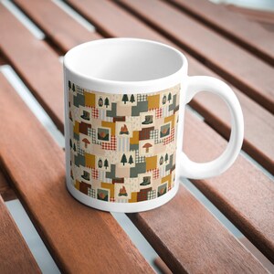 Może przedstawiać: Biały ceramiczny kubek z powtarzającym się wzorem patchworkowych kwadrat&oacute;w. Projekt zawiera ilustracje sosen, ognisk, latarni, grzyb&oacute;w i but&oacute;w w odcieniach musztardowej ż&oacute;łci, leśnej zieleni, czerwieni i beżu.