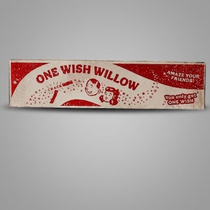 Puede incluir: Una caja rectangular con un dise&ntilde;o en rojo y blanco roto que presenta el texto ONE WISH WILLOW, CRACK, AMAZE YOUR FRIENDS!, y You only get ONE WISH. El gr&aacute;fico incluye ilustraciones de dos rostros sonrientes rodeados de estrellas y s&iacute;mbolos.