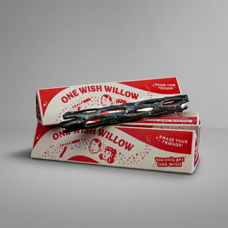 Puede incluir: Un objeto cil&iacute;ndrico oscuro y poroso que descansa sobre dos cajas triangulares apiladas con la etiqueta One Wish Willow. El empaque presenta gr&aacute;ficos rojos y blancos con ilustraciones de ni&ntilde;os, el texto Amaze Your Friends y You only get ONE WISH.