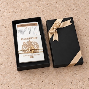 May include: A black gift box containing a white scratch-to-reveal passport card and a boarding pass. The passport card features a gold airplane charm and the text Passport, Scratch to Reveal, and Boarding Pass with details including LAX.