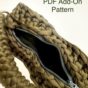 May include: Close-up of a handmade olive green bag with a zipper closure. The bag is made of a thick, braided fabric. The text "PDF Add-On Pattern" is visible in the upper right corner. The bag's interior is black.