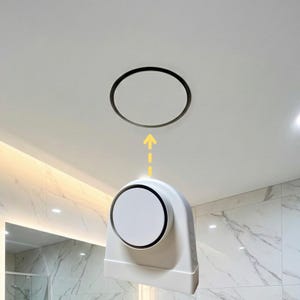 May include: A white ceiling-mounted ventilation system with a circular vent and a matching circular cover. A yellow arrow indicates the direction of airflow. The system is installed in a bathroom with marble-patterned walls.