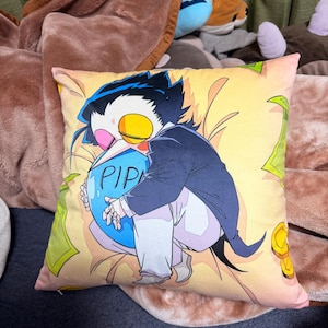 May include: A decorative pillow featuring a cartoon character in a suit, holding a blue orb with the text "PIP". The pillow has a yellow background with green and gold accents. The pillow is surrounded by other plush toys.