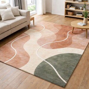 Könnte beinhalten: Rechteckiger Teppich mit abstraktem Design in Rosa-, Beige- und Grüntönen. Weiße, wellenförmige Linien bilden ein Muster. Der Teppich liegt auf einem Holzboden.