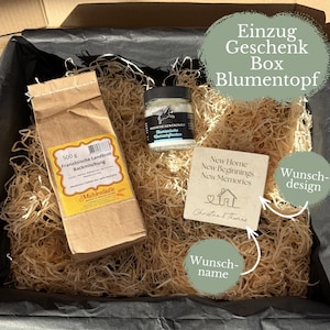 Könnte beinhalten: Eine Geschenkbox mit einer 500g Papiertüte Backmischung, einem kleinen Glas mit Meersalzflocken und einem quadratischen Steinuntersetzer, bedruckt mit dem Text New Home New Beginnings New Memories sowie einem Haus-Symbol und dem Namen.