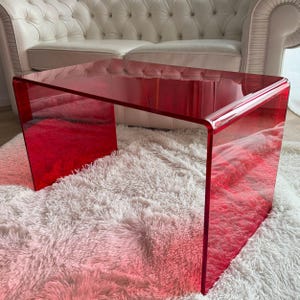 Könnte beinhalten: Ein rechteckiger Couchtisch aus einem einzigen, durchgehenden Stück durchscheinendem rotem Acryl. Der Tisch verfügt über ein Wasserfall-Kantendesign mit glatten, abgerundeten Ecken und einer glänzenden, transparenten Oberfläche, die Licht durchlässt.
