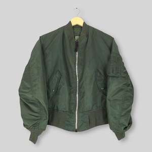 May include: A dark green bomber jacket with a full-length silver zipper, two front pockets, and a pocket on the left sleeve. The jacket has a ribbed collar, cuffs, and hem. The jacket is hanging on a wooden hanger.