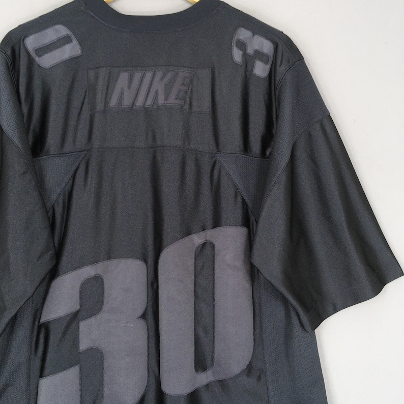 Puede incluir: Camiseta de f&uacute;tbol Nike negra con el n&uacute;mero 30 en gris en la parte delantera. El logotipo de Nike est&aacute; centrado en el pecho. Parches grises en los hombros. La camiseta tiene cuello redondo y mangas cortas.