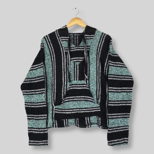 May include: A black, teal, and white striped Baja hoodie with a front pocket and hood. The woven fabric is hanging on a wooden hanger. The hoodie has long sleeves and a relaxed fit, against a neutral background.