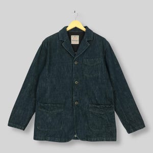 Può includere: Una giacca in denim blu scuro con colletto a revers, tre bottoni frontali e tre tasche applicate. L'etichetta interna sul collo riporta la scritta "PERSON'S" in bianco su sfondo nero. La giacca è dotata di maniche lunghe.