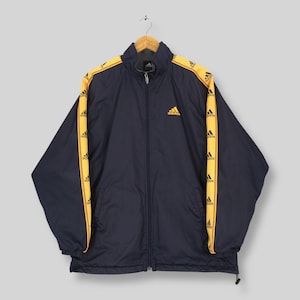 May include: Navy blue Adidas track jacket with yellow stripes featuring the Adidas logo. The jacket has a full zipper, a stand-up collar, and the Adidas logo on the chest. A vintage athletic jacket.