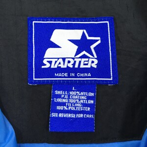 May include: Close-up of a blue Starter brand tag with white text and logo. The tag reads "STARTER" and "MADE IN CHINA". Below the main tag is a smaller tag with fabric information.