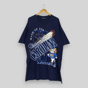 May include: Navy blue t-shirt featuring a basketball graphic with the words "Go Carolina" and "Tar Heels." The design includes a basketball, a basketball court diagram, and a cartoon mascot. The shirt is made in the USA.