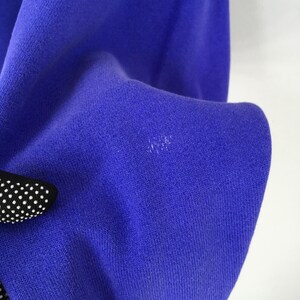 May include: Close-up of a vibrant blue fabric, possibly a piece of clothing. The texture of the material is visible, with a slight sheen. A small section of a black and white polka-dotted object is visible in the lower left corner.