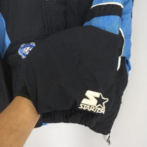 May include: Black and blue vintage Starter jacket with a Carolina logo patch and Starter logo. The jacket has a drawstring at the bottom and a snap closure. The sleeves are black with blue and white accents.