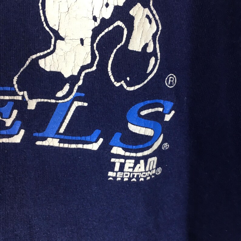 May include: Close-up of a navy blue garment with white and blue lettering. The word "TEAM" is visible, along with the word "EDITION" below it. The garment has a distressed, vintage look.