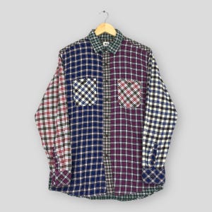 Könnte beinhalten: Ein langärmeliges Flanellhemd mit Patchwork-Design. Das Hemd hat eine Mischung aus Karomustern in Blau, Burgunderrot und Weiß mit zwei Vordertaschen. Kragen und Manschetten haben ein kontrastierendes grün-weißes Muster.