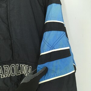 May include: Black jacket with blue and black striped sleeve detail. The word "AROLINA" is printed in white on the jacket. The jacket is made of a shiny material.