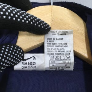 Pu&ograve; includere: Primo piano di un'etichetta di abbigliamento blu navy con testo bianco e un logo Nike. L'etichetta include le istruzioni di lavaggio, la taglia M e il testo "FABRIQUE EN THAILANDE". Il capo &egrave; realizzato in 100% poliammide.