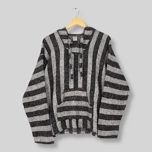 May include: A black and grey striped Baja hoodie with a front pocket and a hood. The hoodie is made of a woven fabric and is hanging on a wooden hanger. The stripes are vertical and evenly spaced.