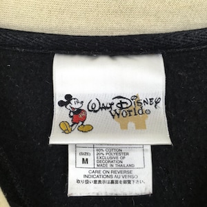 May include: Close-up of a black garment tag with the "Walt Disney World" logo and a Mickey Mouse graphic. The tag also includes fabric content, size "M", and care instructions.