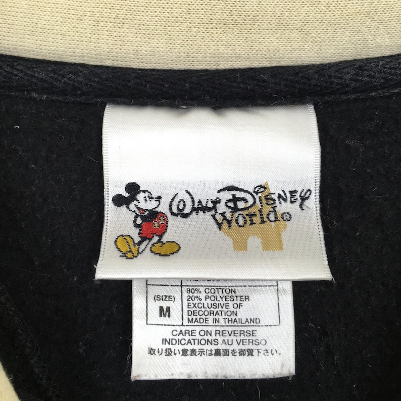 May include: Close-up of a black garment tag with the "Walt Disney World" logo and a Mickey Mouse graphic. The tag also includes fabric content, size "M", and care instructions.