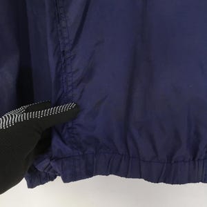 Pu&ograve; includere: Primo piano di una giacca blu navy. La giacca ha un orlo arricciato e una cucitura visibile verticalmente. Il tessuto sembra essere leggero. La giacca &egrave; di colore pieno.