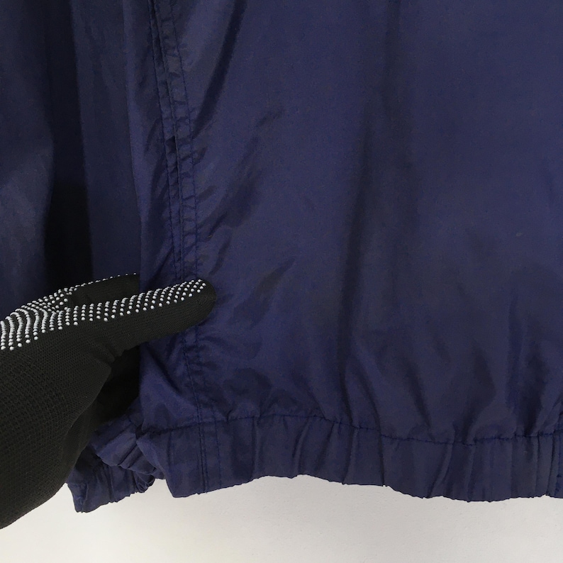 Pu&ograve; includere: Primo piano di una giacca blu navy. La giacca ha un orlo arricciato e una cucitura visibile verticalmente. Il tessuto sembra essere leggero. La giacca &egrave; di colore pieno.