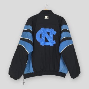 May include: Black and blue Starter jacket with a large light blue "NC" logo on the back. The jacket has blue and white stripes on the sleeves and a Starter logo on the chest.
