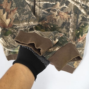 May include: Camouflage zip-up hoodie with brown cuffs. The jacket features a woodland camouflage pattern in shades of brown, green, and tan. The cuffs are a solid brown colour.