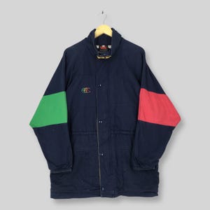 May include: A navy blue jacket featuring a high collar, a front button closure, and long sleeves with color-blocked panels. The left sleeve has a green panel, the right sleeve has a red panel, and a small embroidered logo is on the chest.