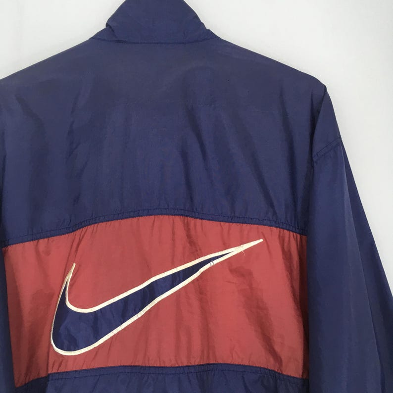 Pu&ograve; includere: Giacca blu navy e rossa con un grande logo Nike bianco e blu navy. La giacca ha un collo alto e una striscia rossa sul petto con il logo Nike. La giacca &egrave; realizzata in materiale leggero.