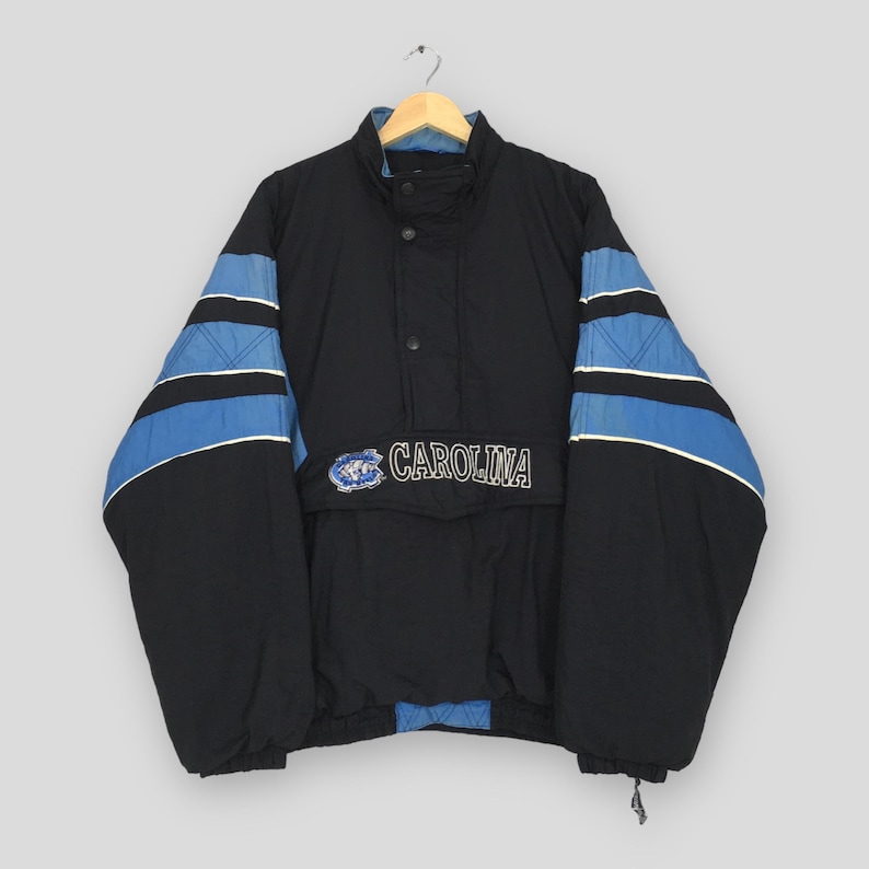 May include: Black and blue Carolina jacket with a high collar and a front pocket. The sleeves feature blue stripes with white accents. The word "CAROLINA" is embroidered on the front.