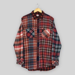 Può includere: Una camicia a maniche lunghe con bottoni caratterizzata da un design patchwork con vari motivi a quadri rossi, blu, neri e bianchi. La camicia include un colletto, un'abbottonatura frontale e due tasche sul petto con patta. Un'etichetta bianca riporta UNIQLO.