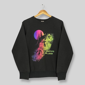 May include: Black sweatshirt with a colorful graphic of skiers on a mountain, a vibrant sunset, and the text "Vancouver Canada". The design features neon pink, yellow, and purple hues, creating a retro aesthetic.