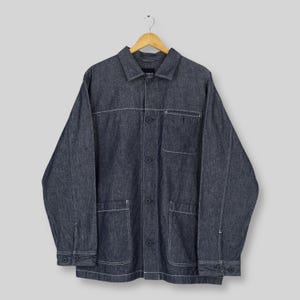 以下が含まれることがあります： 白いステッチが施された濃い青色のデニムジャケット。 ジャケットはボタン留め、胸ポケット2つ、下ポケット2つ。 木製ハンガーにかかっています。