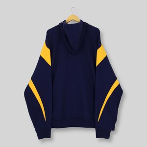 May include: A navy blue hoodie with yellow panels on the sleeves. The hooded sweatshirt is displayed on a wooden hanger. The background is a plain, neutral colour. The design is simple and classic.