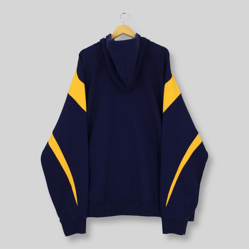 May include: A navy blue hoodie with yellow panels on the sleeves. The hooded sweatshirt is displayed on a wooden hanger. The background is a plain, neutral colour. The design is simple and classic.
