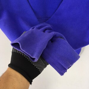 May include: Close-up of a vibrant purple hoodie. The ribbed cuffs and hem are a darker shade of purple. The sleeve is pulled back, revealing a black glove with white polka dots.