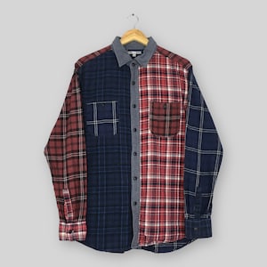 May include: A long-sleeved button-down shirt featuring a colour-blocked plaid pattern. The garment combines panels of dark navy blue and deep red tartan fabric. It includes a grey collar, a central button placket, and two chest pockets with flaps.
