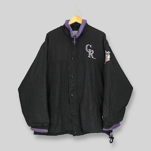 May include: Black baseball jacket with purple and white details. It has a button-up front, a purple collar, and the team logo on the chest. The jacket has a drawstring at the bottom and a team logo patch on the sleeve.