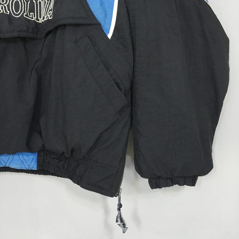 May include: Black and blue jacket with white accents. The jacket features a front pocket and a zipper closure. The word "ROLINA" is visible in white lettering on the upper portion of the jacket.